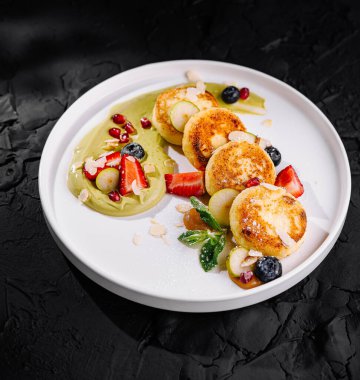 Elegant cheese pancakes adorned with berries and mint on a white plate, black background