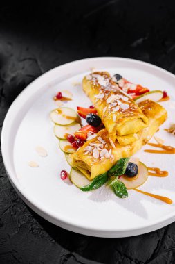 Artfully plated crepes with fruit toppings and caramel drizzle on a dark background