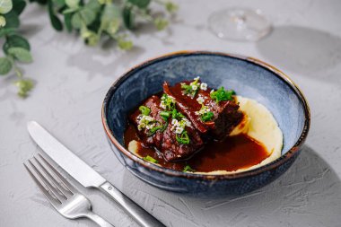 Tender beef ribs in a rich glaze, served with smooth polenta on a stylish plate, perfect for gourmet dining