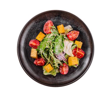 Top view of a colorful mixed vegetable salad on a rustic black plate, isolated on white