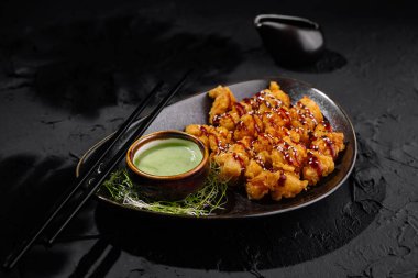 Delicious crispy fried chicken with sesame seeds and sauces on a slate plate, dark background