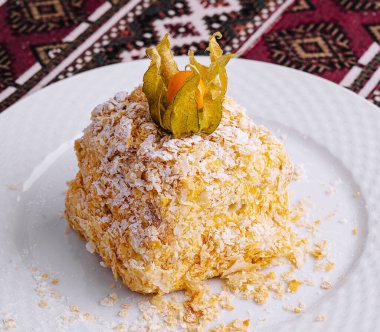 Delectable sweet napoleon cake topped with dried fruit, served on a white plate with an intricate patterned background