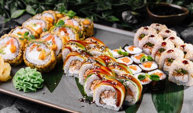 Appetizing array of sushi rolls garnished with sauces, ginger, and wasabi on a slate tray