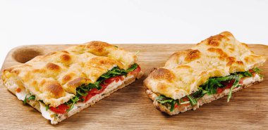 Kesme tahtasının üzerinde sebze ve peynirli dilimlenmiş İtalyan panini, beyaz arka planda izole edilmiş.