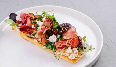 Beyaz bir tabakta prosciutto, feta, domates ve roka ile süslenmiş nefis bruschetta.