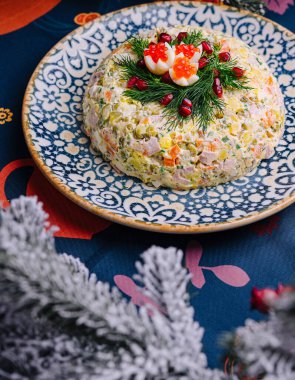 Renkli olivier salatası, desenli bir tabakta, Noel sofrası için süslenmiş.