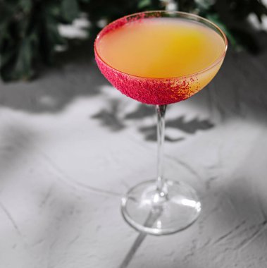 Stylish cocktail glass with a vibrant sugar rim, presented on a sleek, textured backdrop