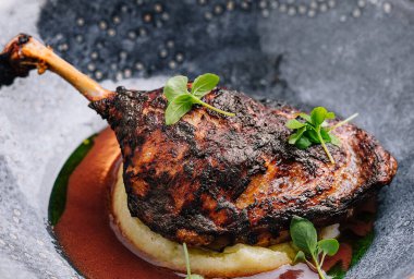 Kızarmış ördek bacağı. Püreden bir yatakta servis ediliyor. Süslü otlar, güzel bir yemek sunumu.