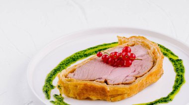 Kırmızı kuşüzümü ve yeşil soslu beyaz tabakta servis edilen zarif sığır eti Wellington.