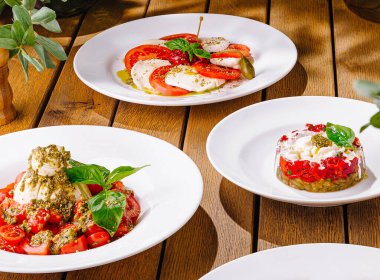 Variety of tomato and cheese dishes artfully presented on white plates, with rustic wood table backdrop