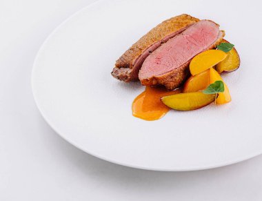 Lezzetli ördek göğsünün, saf beyaz arka planda renkli sebzelerle güzel bir yemek sunumu.