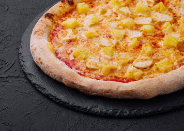 Koyu arkaplanda ananas ve jambon soslu Hawaii pizzasının yakın çekimi.