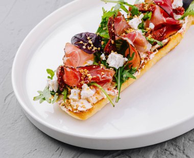 Beyaz bir tabakta prosciutto, feta, domates ve roka ile süslenmiş nefis bruschetta.