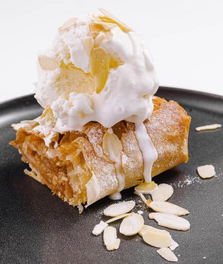 Elmalı turta, vanilyalı dondurma ve badem, modern siyah tabakta servis edilir.