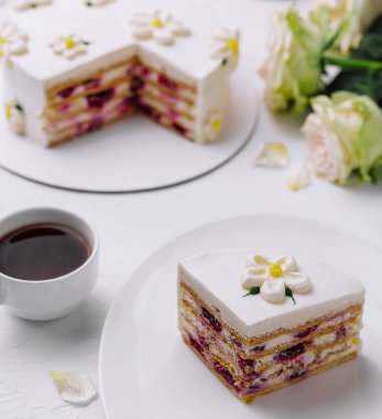 Bir fincan kahveyle birlikte yenilebilir çiçeklerle süslenmiş güzel katmanlı bir pastanın dilimi.