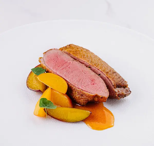 stock image Fine dining presentation of succulent duck breast paired with colorful vegetables on a pristine white background