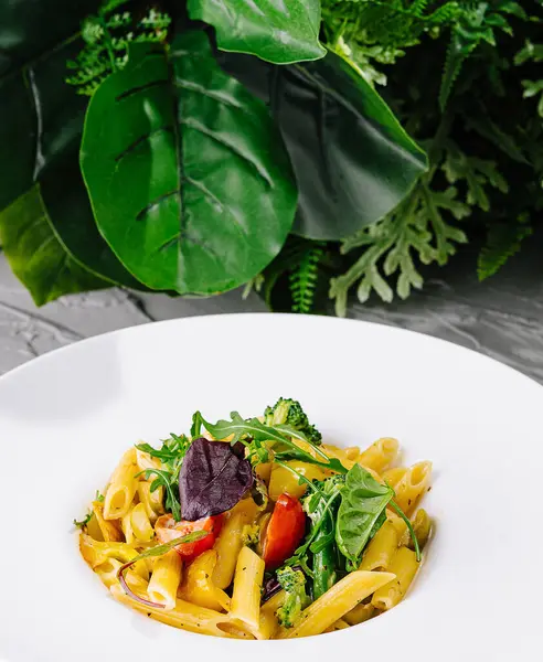 stock image Penne pasta mixed with leafy greens, tomatoes, and herbs, served on a stylish white plate