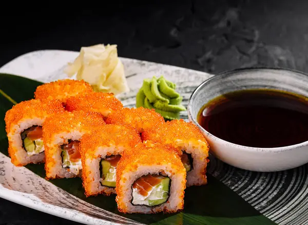 stock image Appetizing california roll sushi topped with tobiko, served with soy sauce, ginger, and wasabi on a dark slate