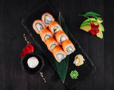 Somon, avokado ve krem peynirli siyah taş tabakta Philadelphia suşi rulosu.