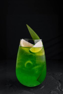 Yeşil kokteyl limon dilimleri ve taze yapraklı garnitürle bir barda duruyor.
