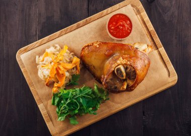 Tahta bir tahtada salata, lahana turşusu ve sos ile çıtır domuz budu servis edilir.