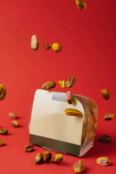 stock image Pistachio nuts falling from the sky onto packaging against a red background