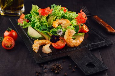 Siyah tahta masada karides, avokado ve kiraz domatesli taze salata servis edilir.