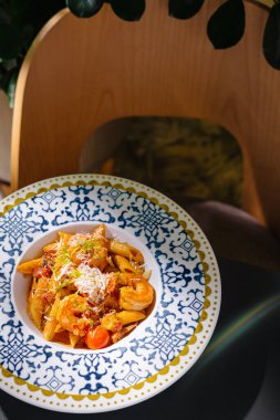 Mavi ve beyaz tabakta servis edilen karides, domates ve parmesan peynirli makarna tabağı.