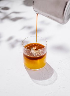 Barmen beyaz arka planda sarı bir kokteyl ile bardağa espresso dolduruyor.