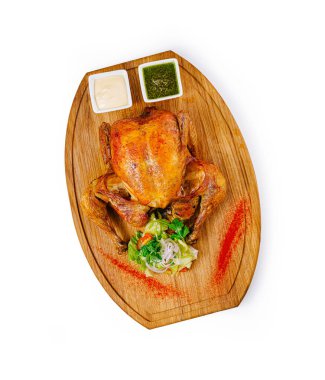 Ahşap kesme tahtasında servis edilen kızarmış tavuk, baharatlar, sebzeler ve soslarla birlikte, beyaz arka planda izole edilmiş.