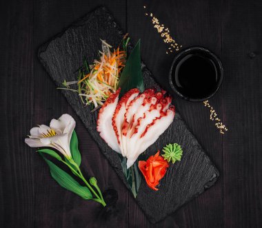Dilimlenmiş ahtapot sashimi soya sosu, wasabi ve zencefilli siyah tahtada servis edilir.