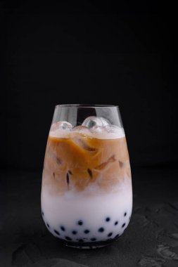 Sütlü buzlu kahve ve tapyoka incileri siyah arkaplanda duruyor.