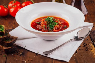 Beyaz kase lezzetli kırmızı borş ile doludur, taze otlarla süslenir ve çavdar ekmeğinin yanında servis edilir.