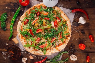 Taze pişmiş roka, kiraz domatesli ve mantarlı pizza kırsal ahşap bir masada malzemelerle çevrili.