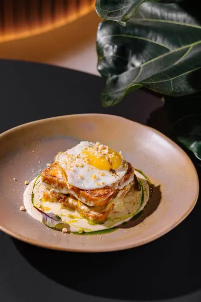 Baharatla süslenmiş, sosla süslenmiş ve restoranda servis edilen kızarmış yumurtalı Croque Madame.