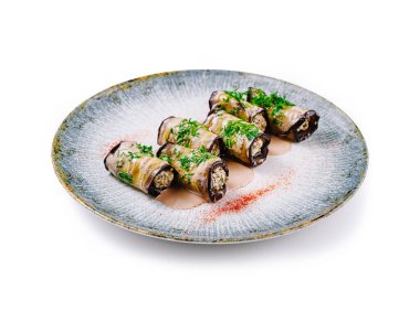 Sos ve baharatla süslenmiş tabakta fındık ve otlarla doldurulmuş lezzetli patlıcan ruloları var.