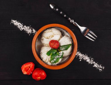 Üç top dondurma bir kasenin içinde duruyor ve siyah ahşap bir masada nane ve çilekle süslenmiş.