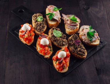Lezzetli bruschetta, domatesler, mozarella, et ezmesi ve ringa balığı siyah taş kesme tahtasının üzerinde.