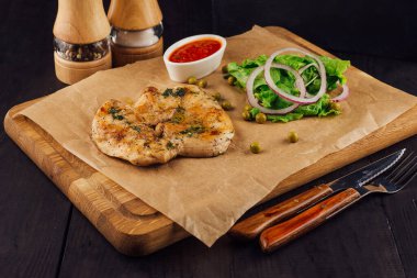 Biberli ızgara tavuk göğsü ve ahşap bir tahtada servis edilen yeşil bezelye, taze salata ve domates sosuyla servis edilmiş otlar.