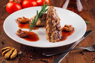 İncir ve biberiyeli ızgara et, biberiye filizi ile süslenmiş beyaz bir tabakta yatıyor.