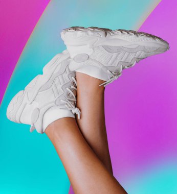 Renkli arka planda beyaz spor ayakkabı giyen kadın bacakları