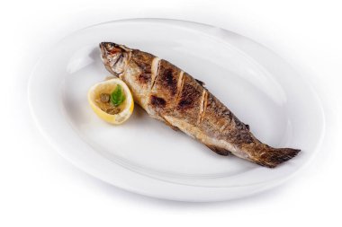 Izgara alabalık, limon ve kapari ile beyaz bir tabakta yatar.