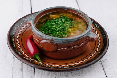 Geleneksel bir kasede servis edilen maydanozlu Ukrayna çorbası ve yanında beyaz ahşap bir masada kırmızı biber.