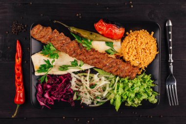 Geleneksel Türk adana kebabı ızgara domates, biber, soğan, salata, maydanoz, lavaş ekmeği ve bulgur pirinç pilavıyla servis ediliyor.