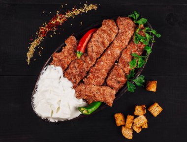 Lule kebabı geleneksel bir tabakta yoğurt, acı biber ve kızarmış ekmekle servis ediliyor.