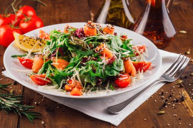 Ahşap masada servis edilen roka, somon, domates ve parmesan peynirli taze salata.