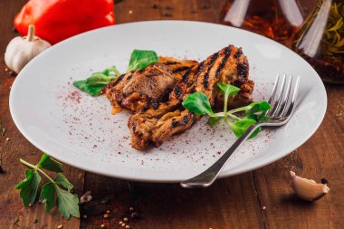 Beyaz tabakta ızgara tavuk göğsü. Ahşap masada yeşil salata servis ediliyor.