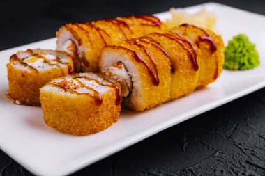 Modern bir restoranda beyaz tabakta servis edilen nefis tempura maki suşi ruloları.