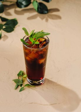 Taze nane yapraklarıyla süslenmiş ferahlatıcı koyu bir kokteyl ile dolu uzun cam bir masanın üzerinde duruyor.