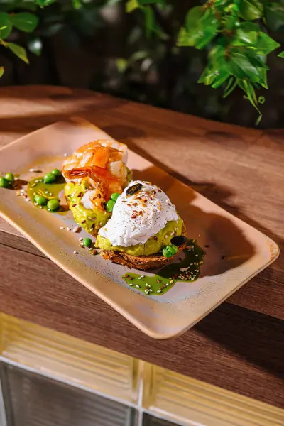 stock image Two slices of avocado toast, one with shrimp and one with a poached egg, are sitting on a plate with a green garnish